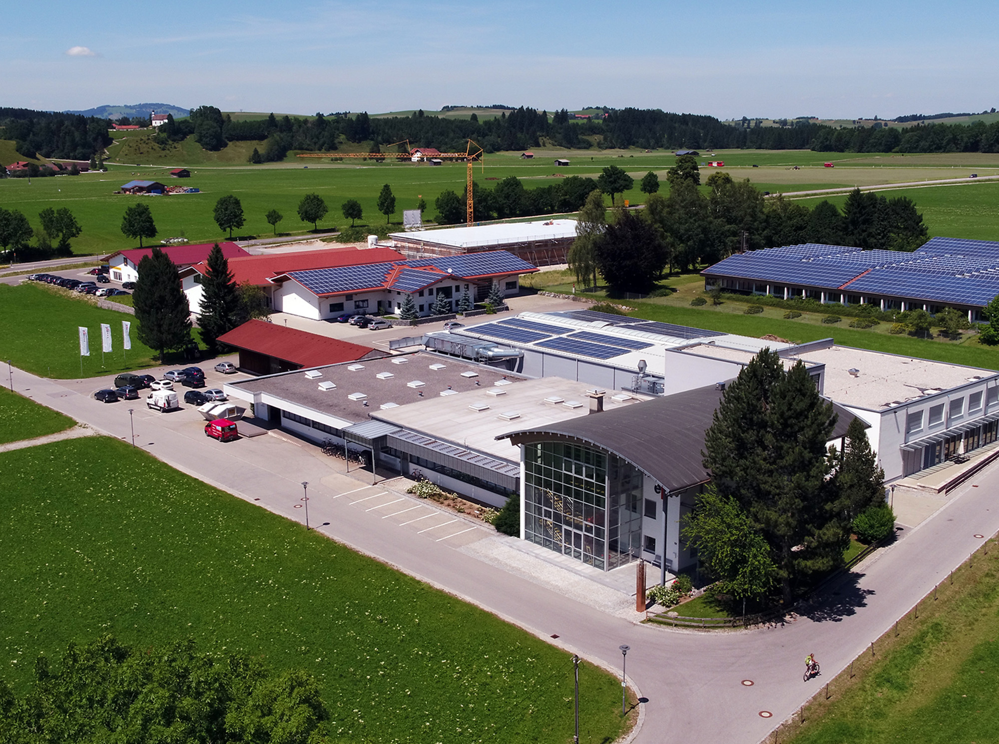 Auf dem Bild ist ein modernes Firmengebäude in ländlicher Umgebung zu sehen, umgeben von grünen Wiesen und Bäumen.